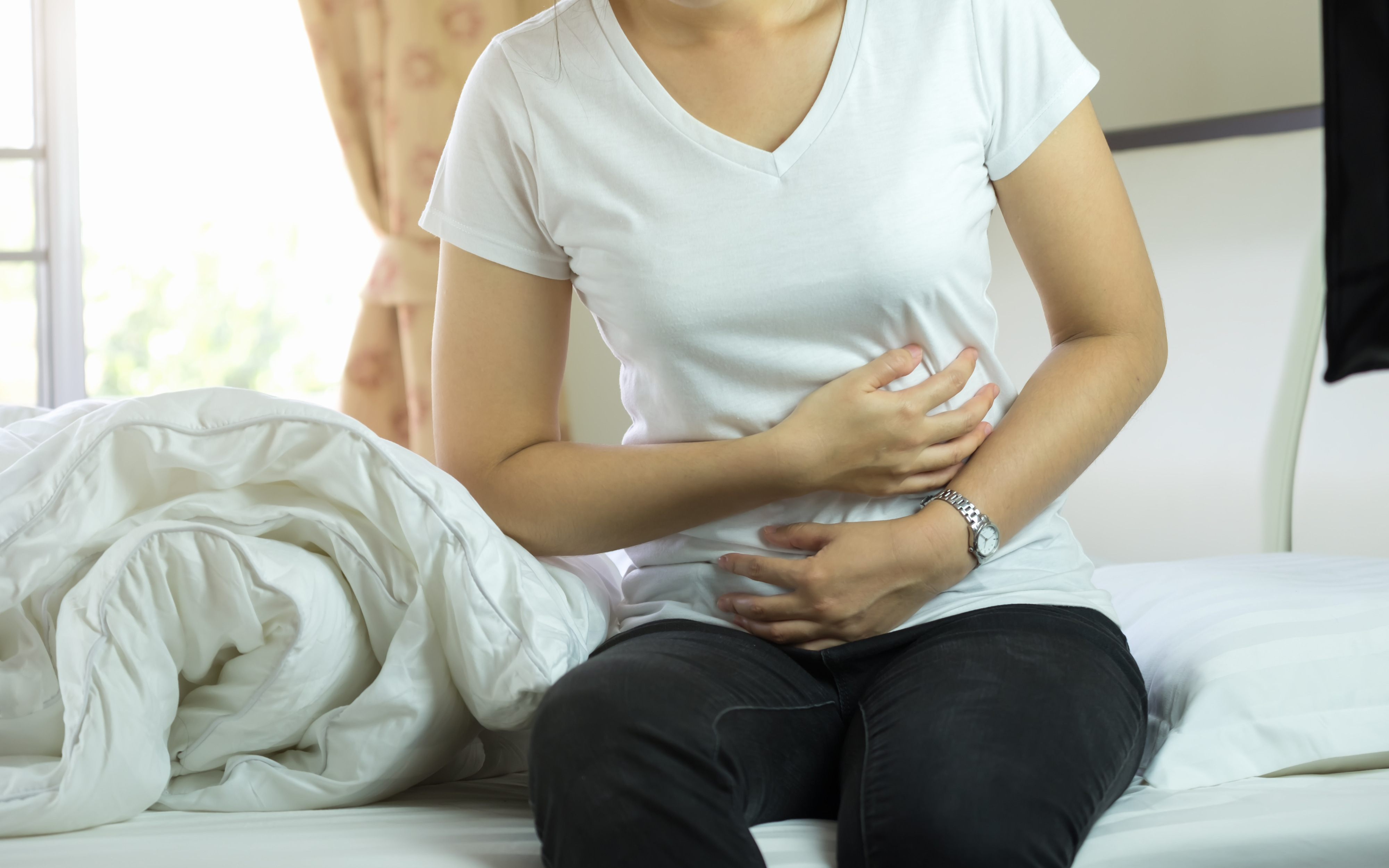 person sitting on bed holding stomach